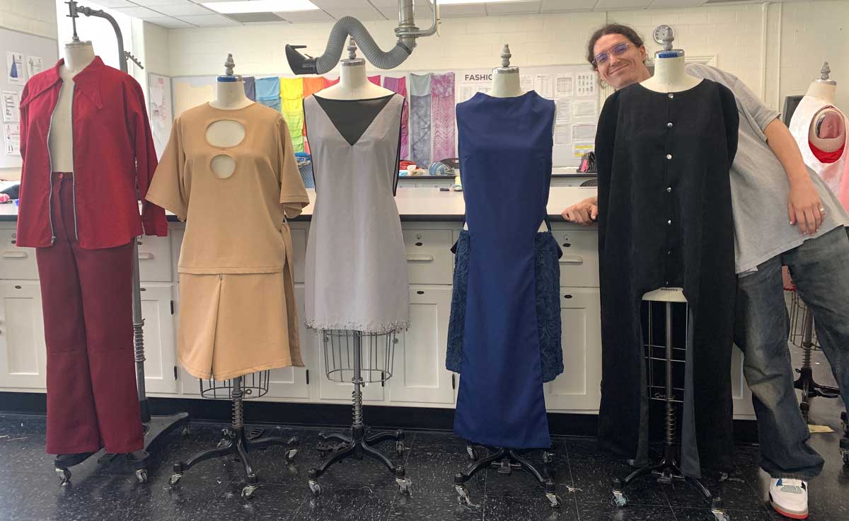 a student posing with his collection of women's clothing