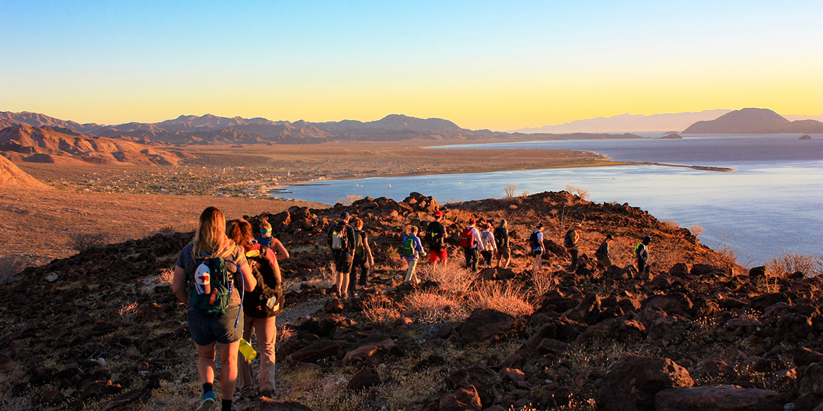 students hiking on rocky trail towards lake